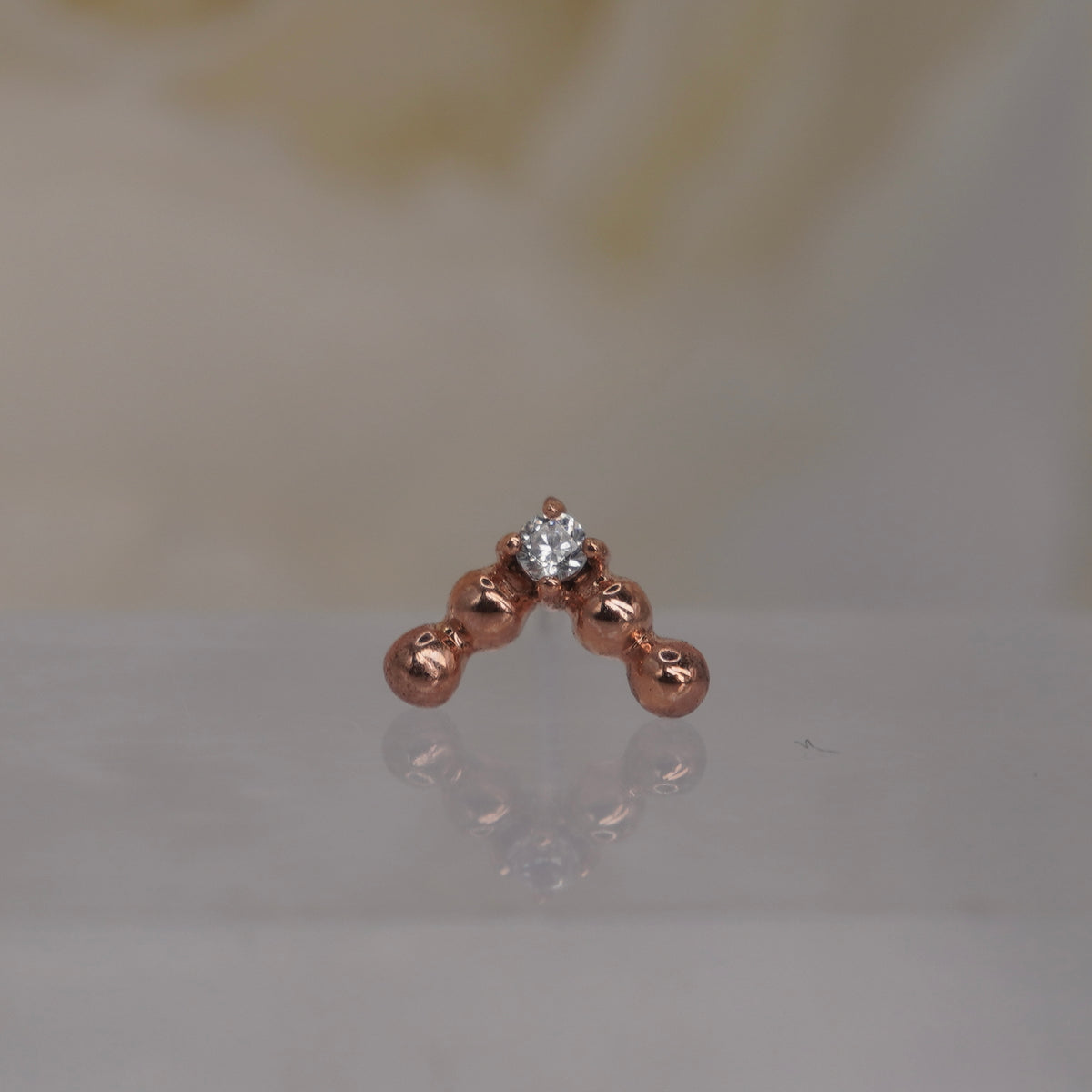 Front view of Buddha Jewelry’s “Voodoo” in 14k rose gold, featuring a structured V of polished gold beads above a single crystal drop.