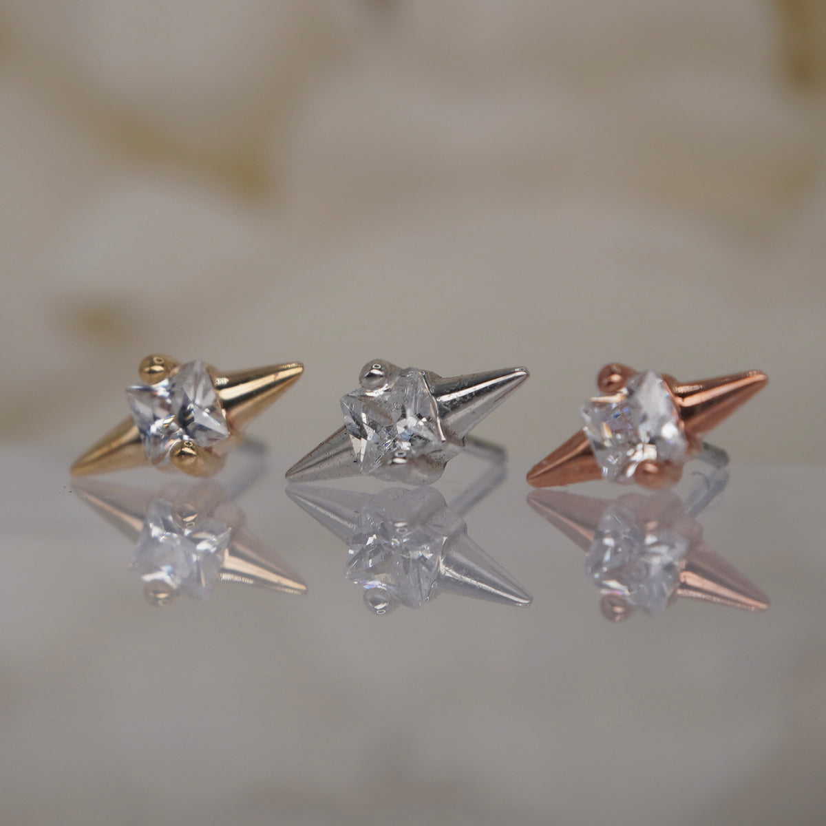 Angled view of Buddha Jewelry’s “Elemental” in 14k yellow, white, and rose gold, showing its symmetrical pointed tips and polished, sculptural profile.