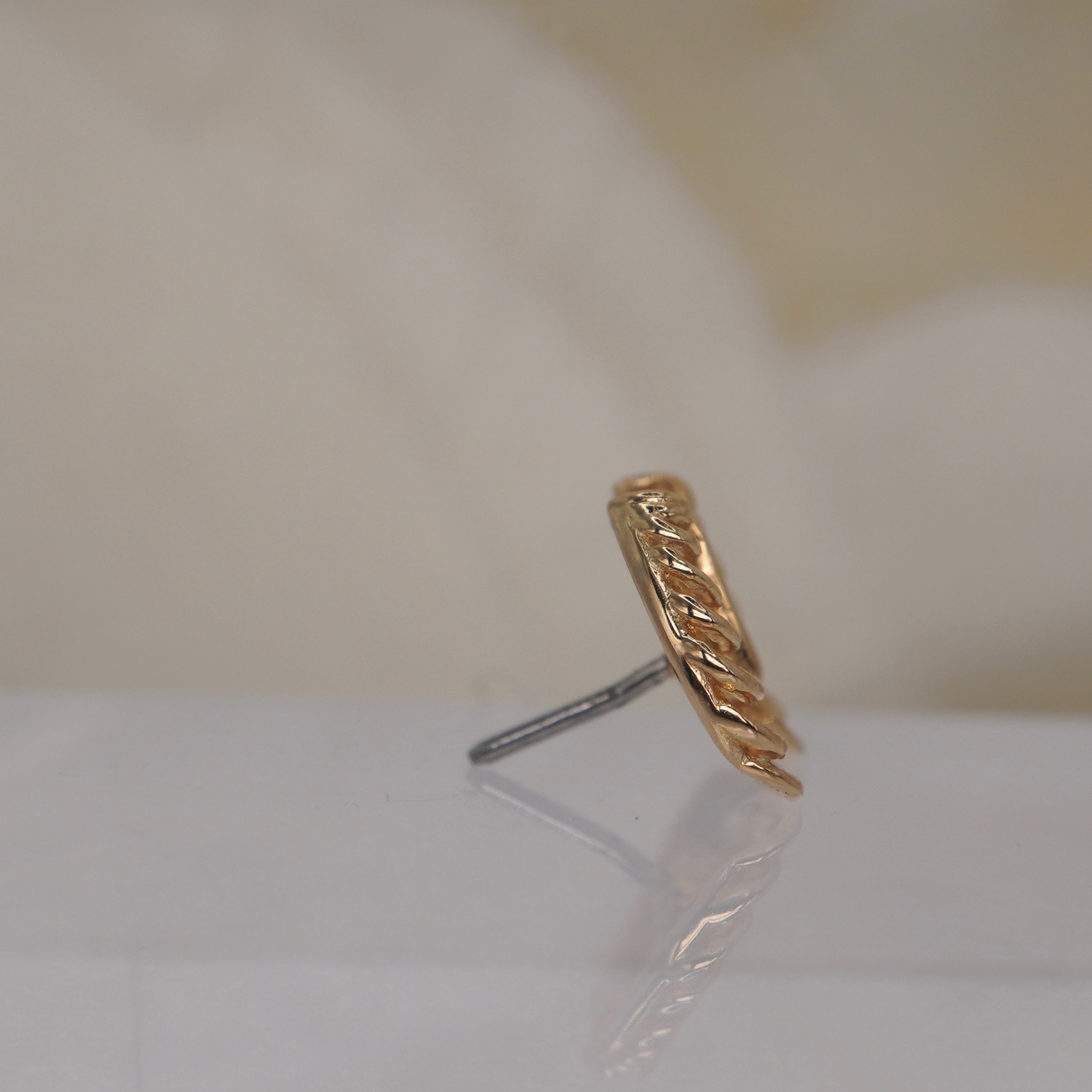 Junipurr 14k "Chest Piece" in yellow gold white gold rose gold black rhodium threadless displayed on a reflective white surface with a soft beige floral background.