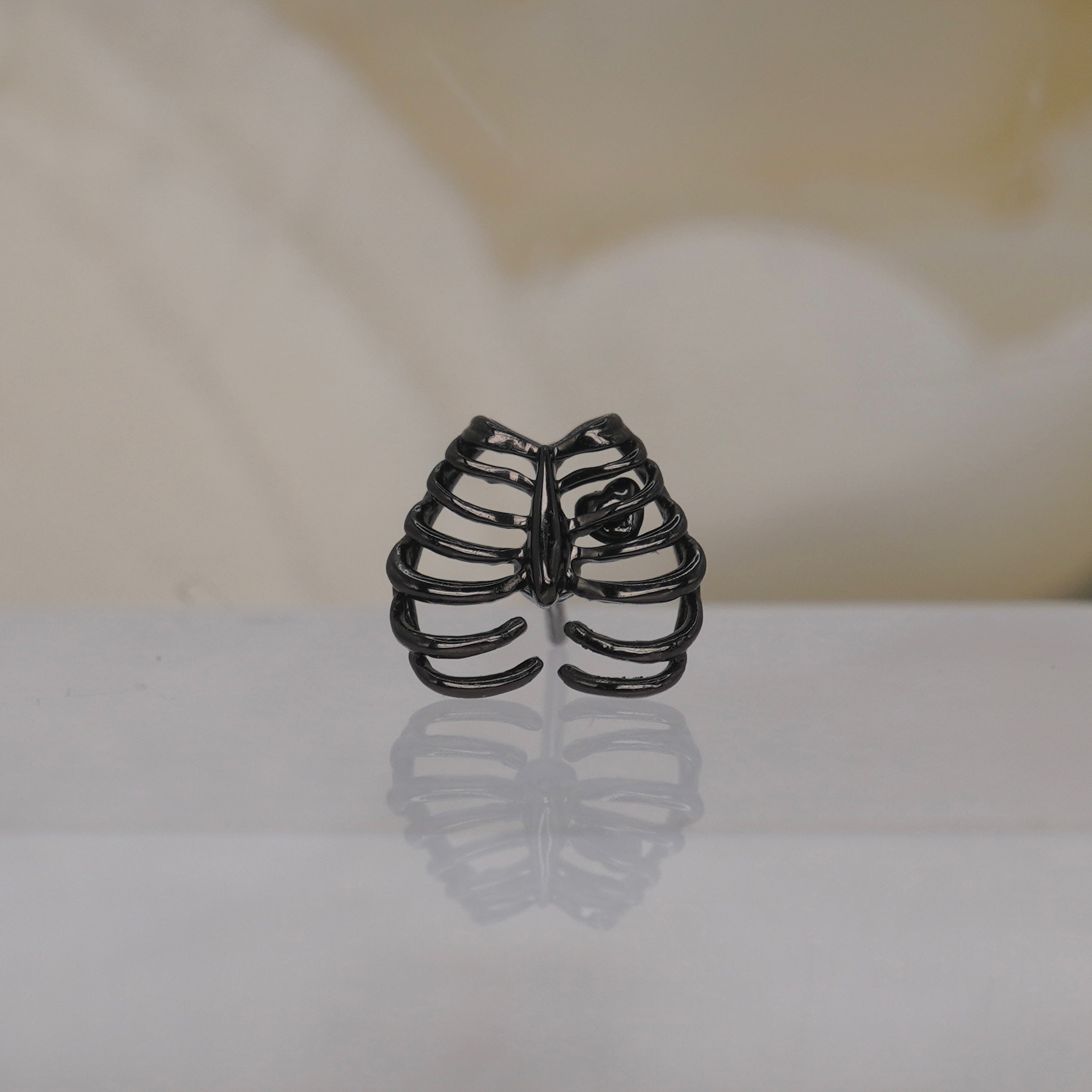 Junipurr 14k "Chest Piece" in black rhodium threadless displayed on a reflective white surface with a soft beige floral background.