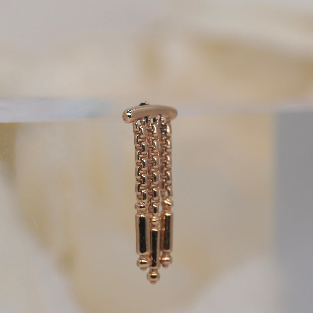 Tempo Hidden Helix textured chains and polished rectangular accents yellow gold closenup photographed against a soft blurred cream floral background.