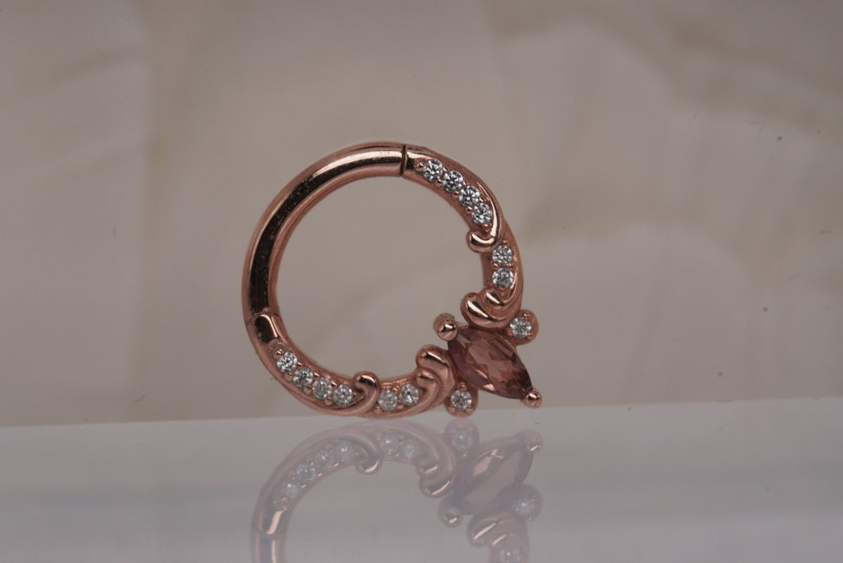 Front view of Buddha Jewelry’s “Coterie” clicker in 14k rose gold, featuring a marquise-cut pink tourmaline accented by delicate crystals and ornate scrollwork.