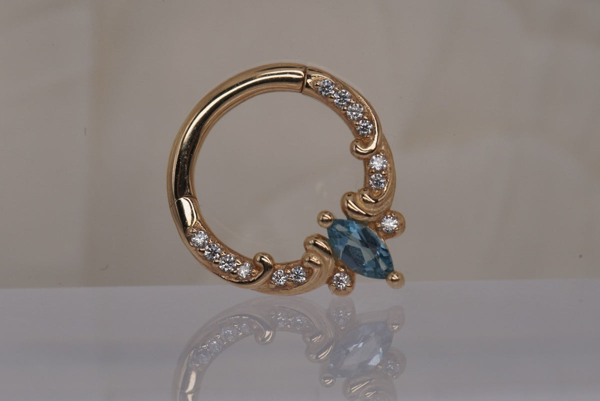 Front view of Buddha Jewelry’s “Coterie” clicker in 14k yellow gold, featuring a marquise-cut London Blue Topaz accented by a delicate row of crystals.