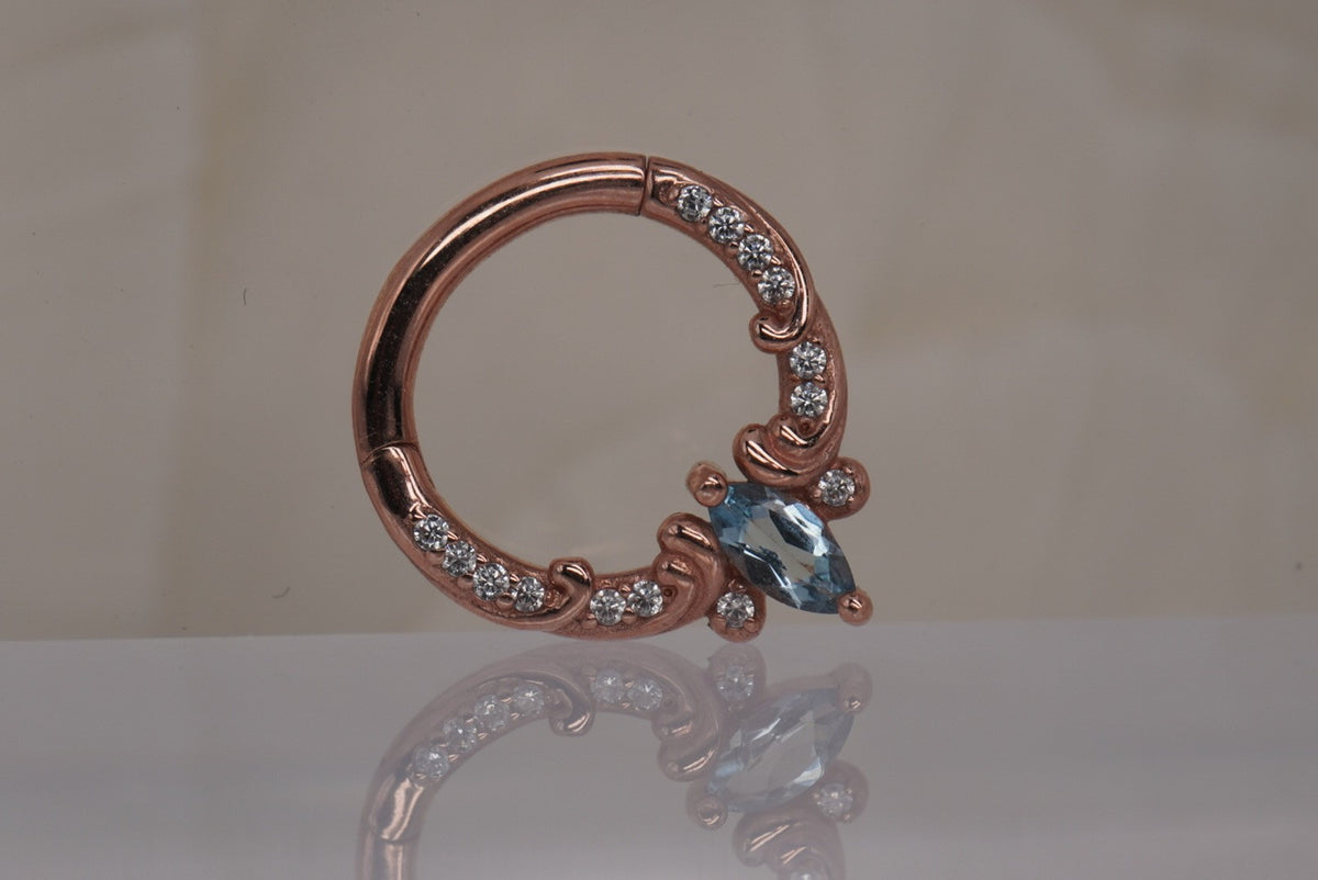 Front view of Buddha Jewelry’s “Coterie” clicker in 14k rose gold, featuring a marquise-cut London Blue Topaz accented by a delicate row of crystals.