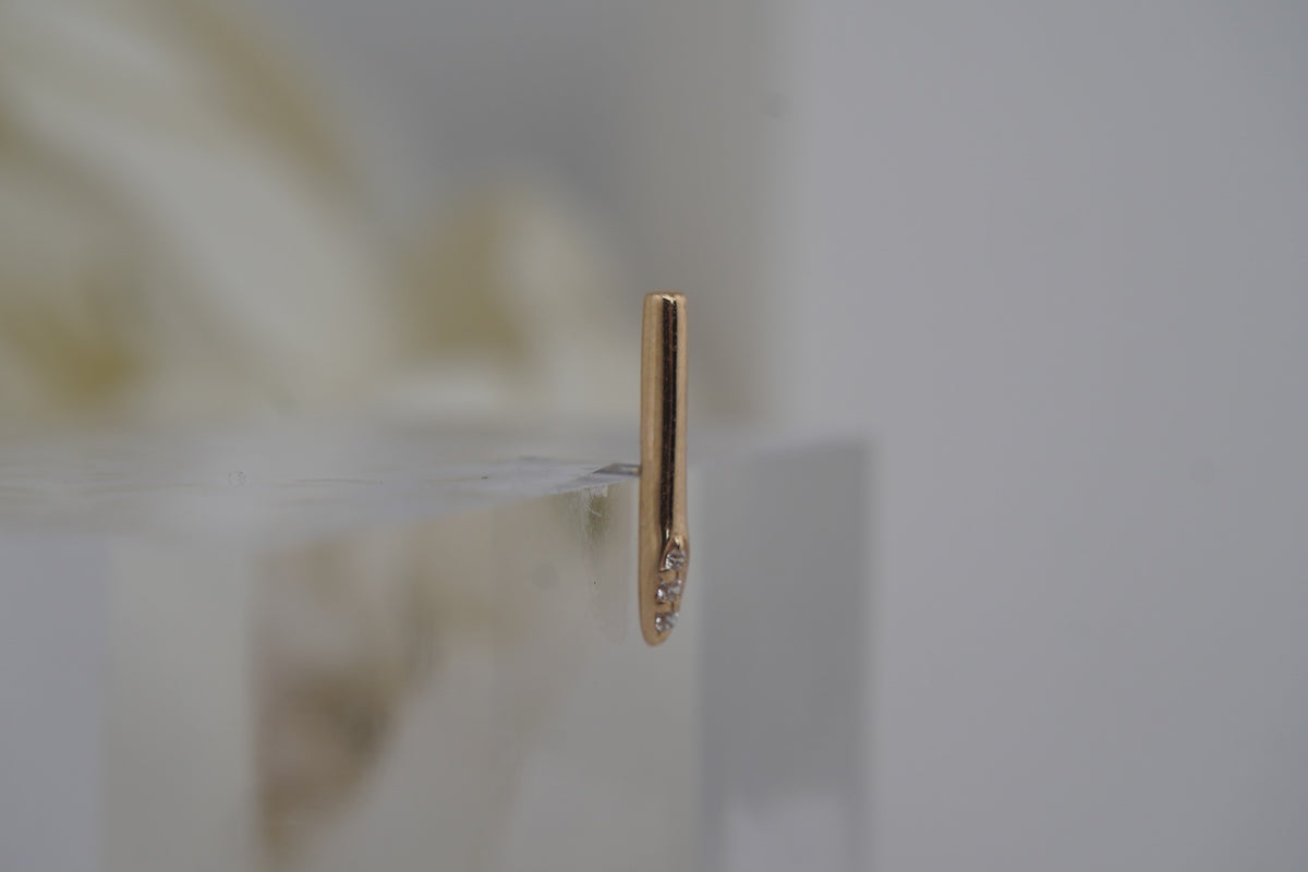 Side view of the needle-inspired design, showing its slim gold profile.