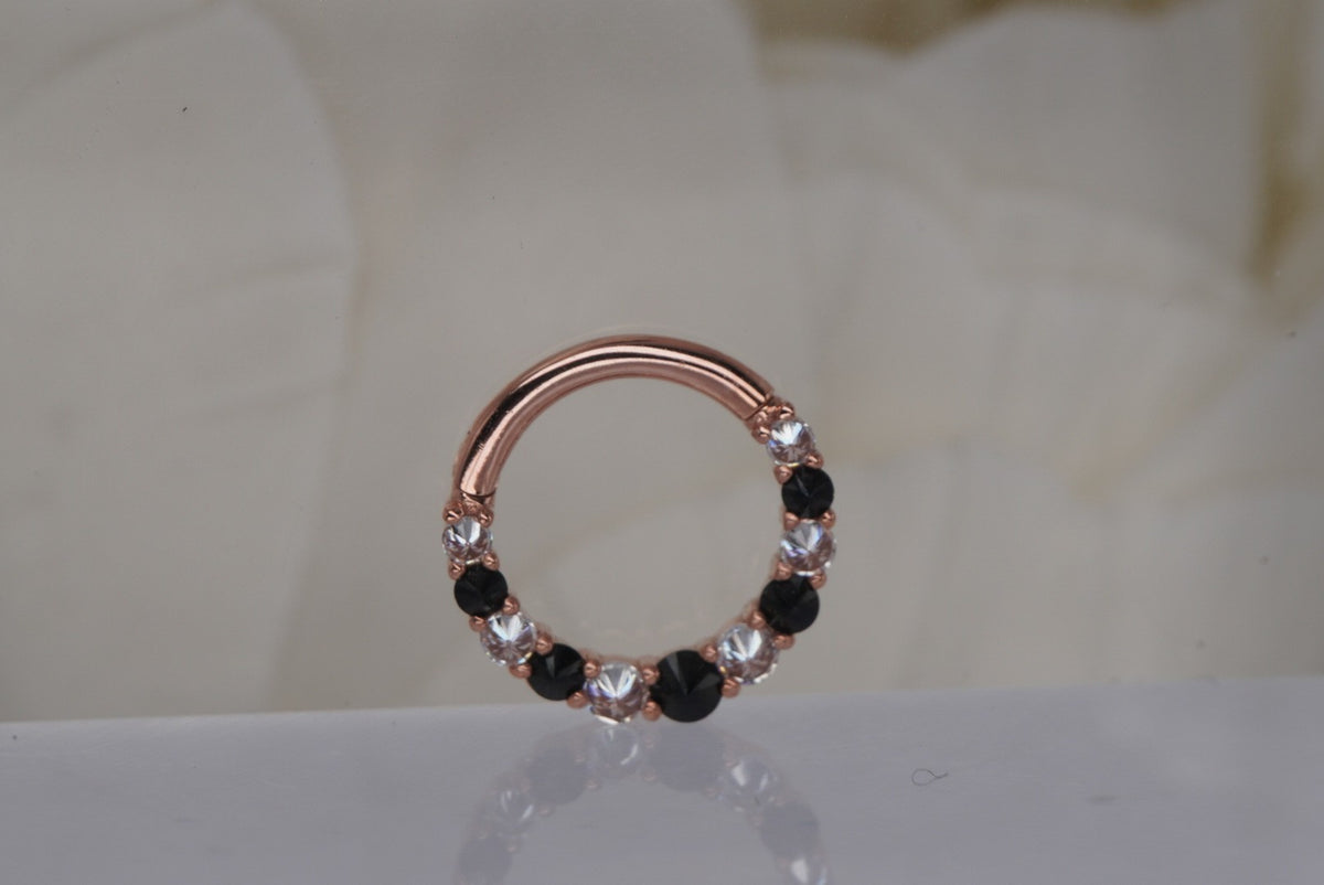 Front view of Buddha Jewelry’s “Eclipse” clicker in 14k rose gold, featuring alternating round black spinel stones and sparkling crystals along the ring.