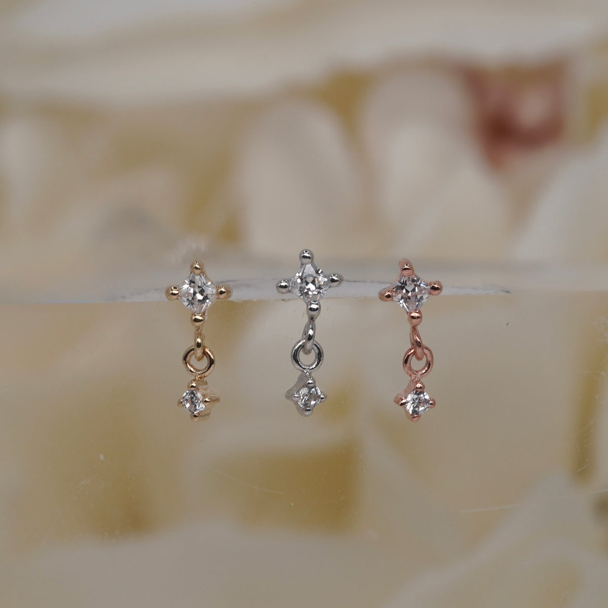 Buddha Jewelry 14k Gold fun and games small princess cut white crystal in a prong setting connected to a dangling small white crystal in a prong setting in Yellow Gold White Gold Rose Gold threadless group view