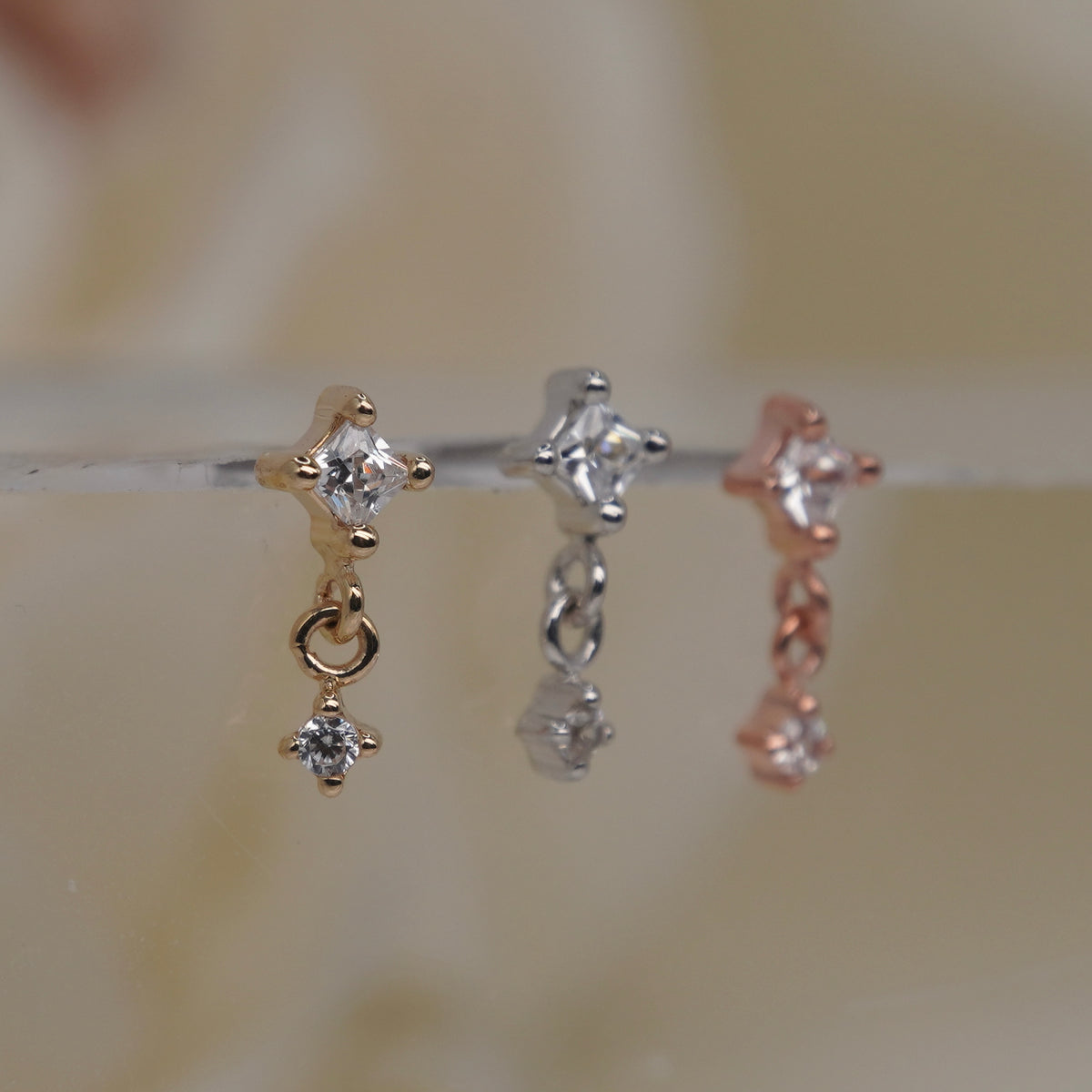 Buddha Jewelry 14k Gold fun and games small princess cut white crystal in a prong setting connected to a dangling small white crystal in a prong setting in Yellow Gold White Gold Rose Gold threadless group side view