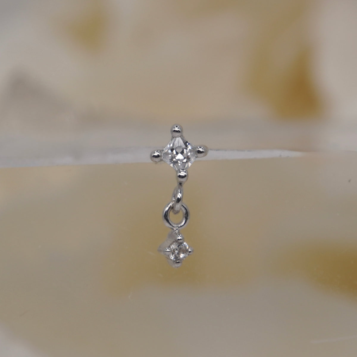 Buddha Jewelry 14k Gold fun and games small princess cut white crystal in a prong setting connected to a dangling small white crystal in a prong setting in White Gold threadless 