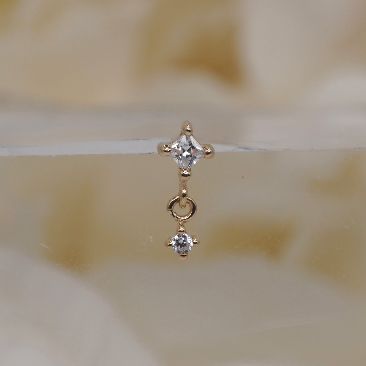 Buddha Jewelry 14k Gold fun and games small princess cut white crystal in a prong setting connected to a dangling small white crystal in a prong setting in Yellow Gold threadless 