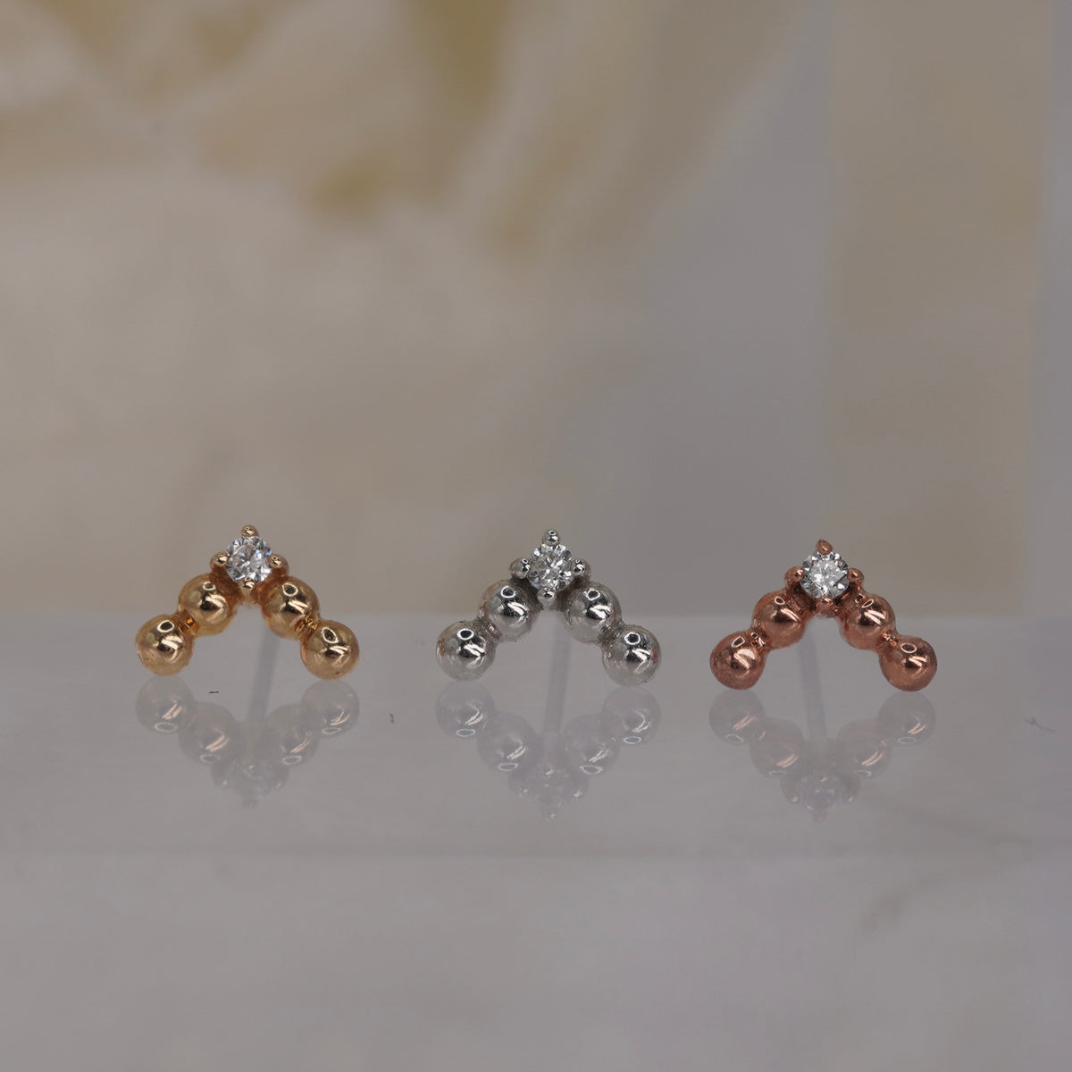Front view of Buddha Jewelry’s “Voodoo” in 14k yellow, white, and rose gold, featuring polished gold beads in a crown-like V with a single crystal drop.