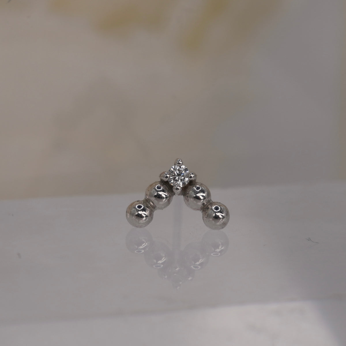 Front view of Buddha Jewelry’s “Voodoo” in 14k white gold, featuring a structured V of polished gold beads above a single crystal drop.