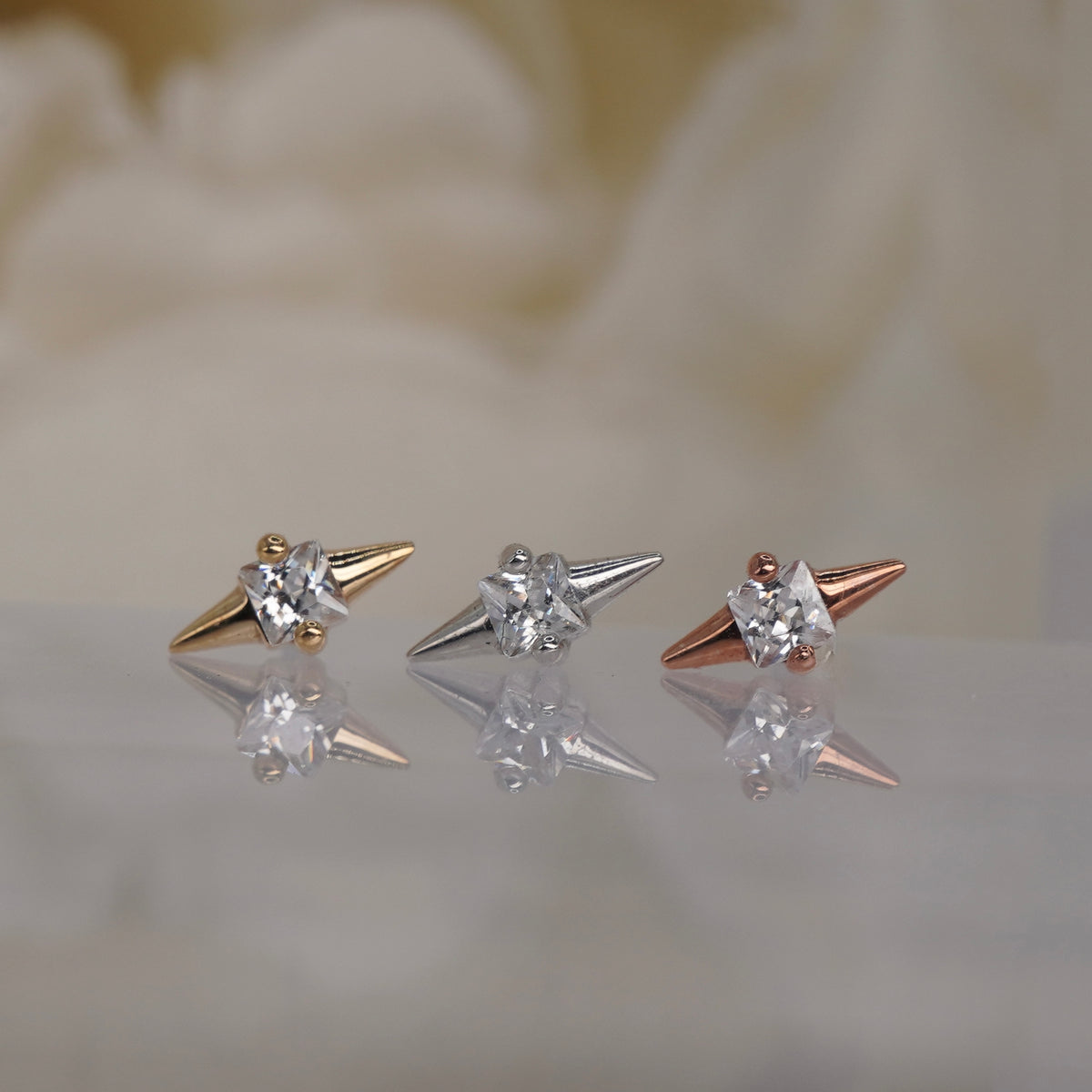 Front view of Buddha Jewelry’s “Elemental” in 14k yellow, white, and rose gold, featuring a square-cut crystal framed by opposing pointed gold tips.
