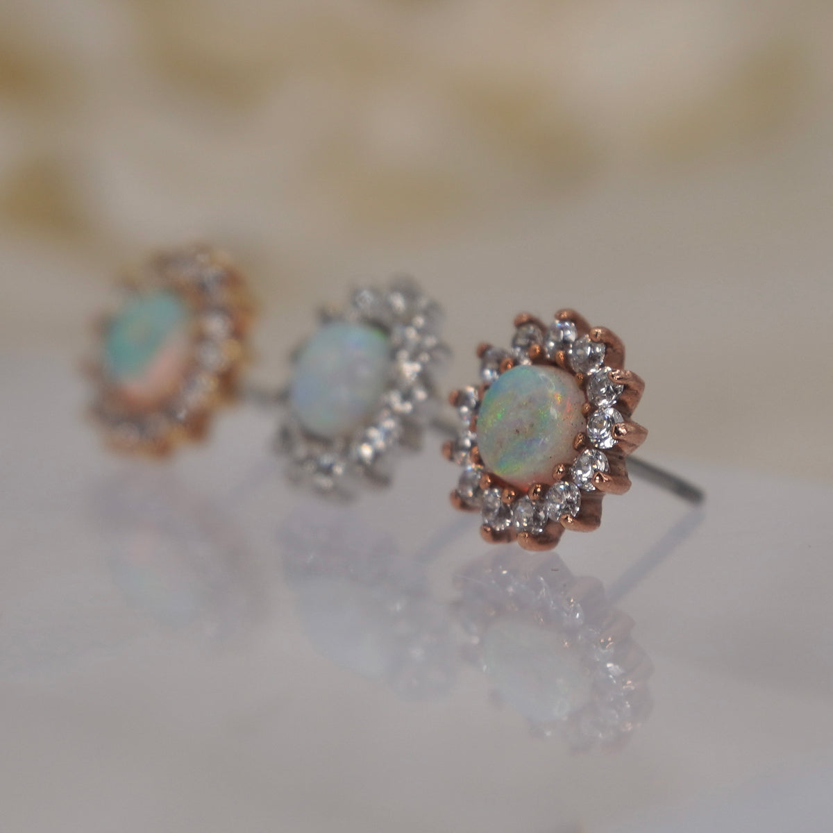 Angled view of Buddha Jewelry’s “Delphine” in 14k yellow, white, and rose gold, showing the opal’s flashes of color and dimensional floral silhouette.