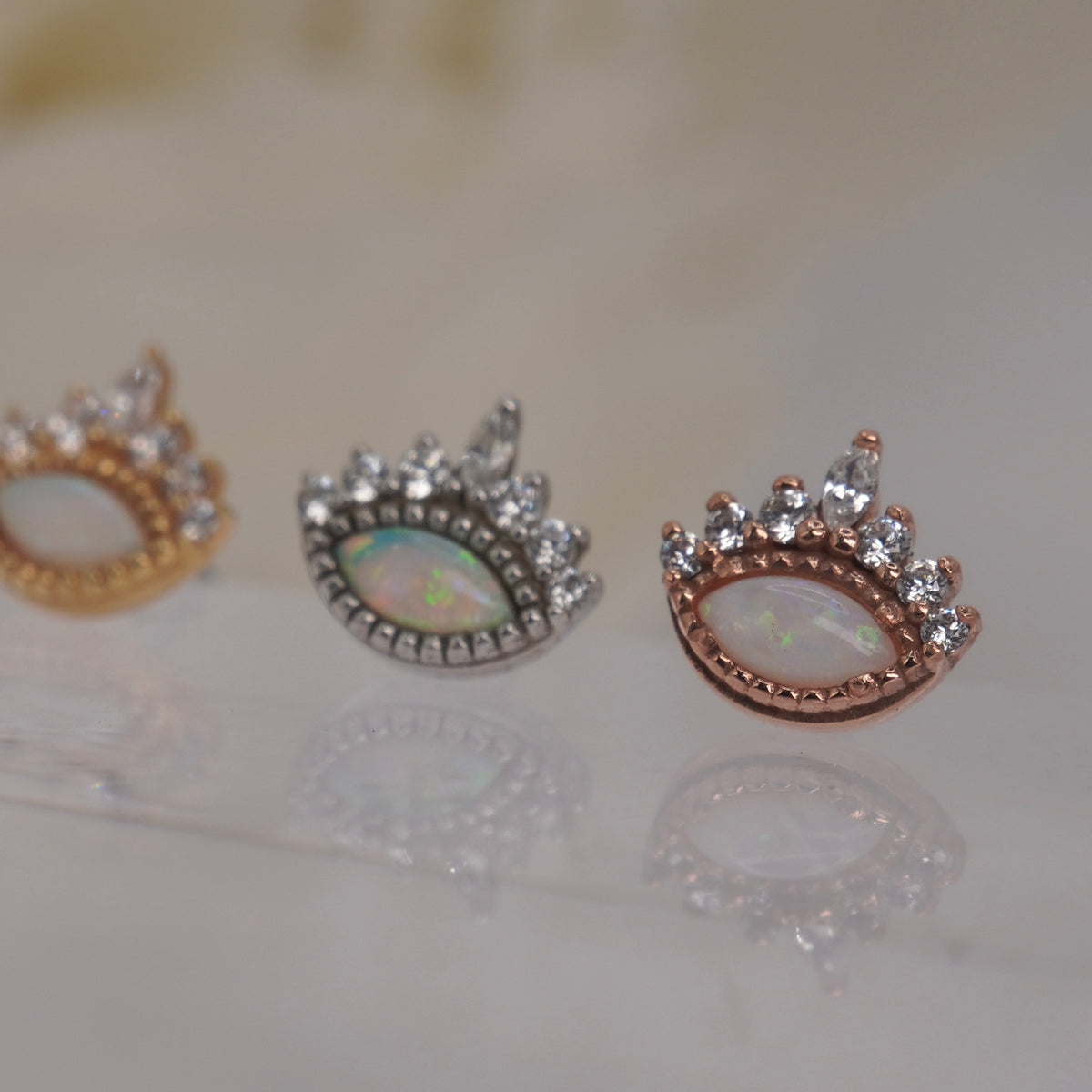 Angled view of Buddha Jewelry’s “Enchant” in 14k yellow, white, and rose gold, showing the opal’s rainbow sheen and dimensional crystal crown.