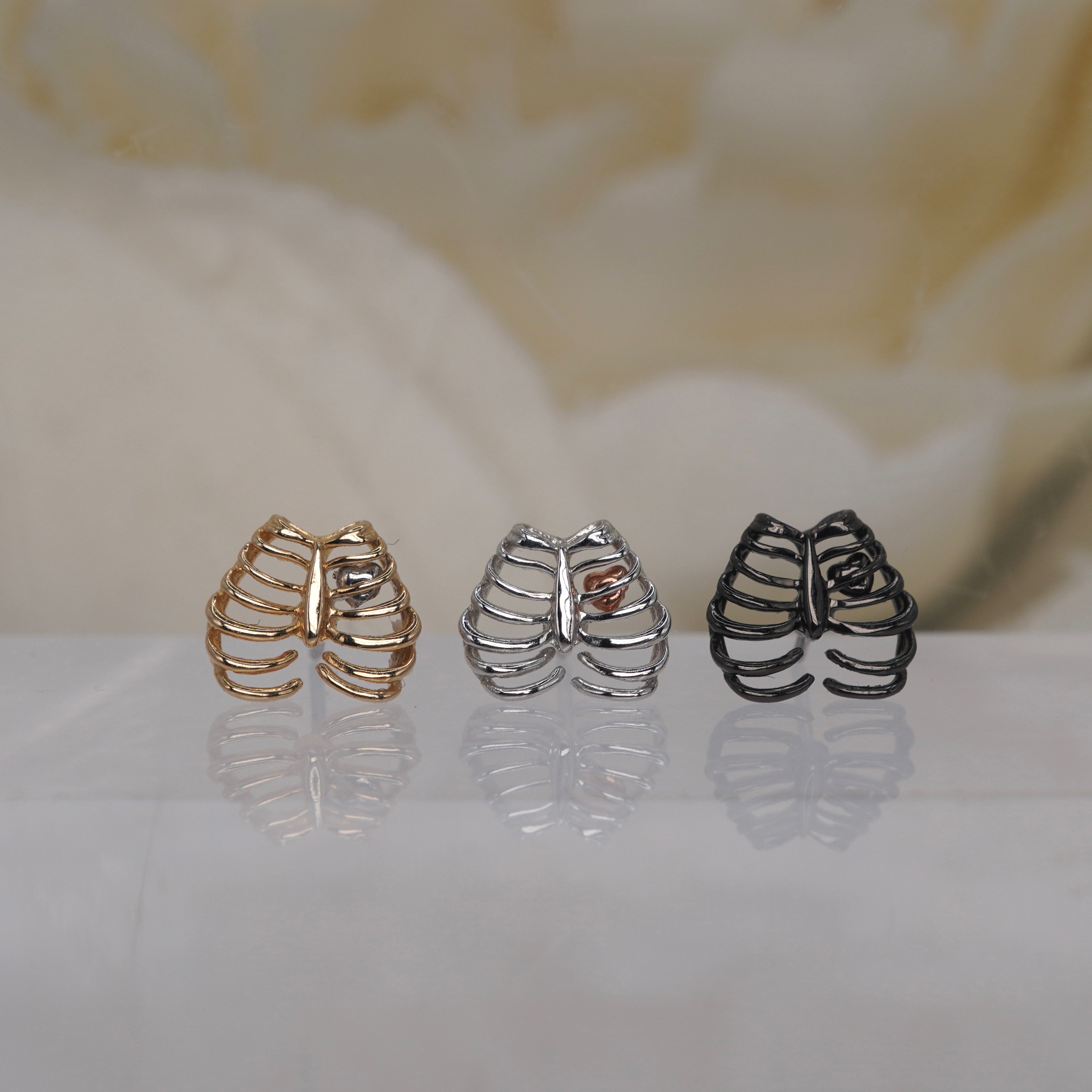 Junipurr 14k "Chest Piece" in yellow gold white gold rose gold black rhodium threadless displayed on a reflective white surface with a soft beige floral background.