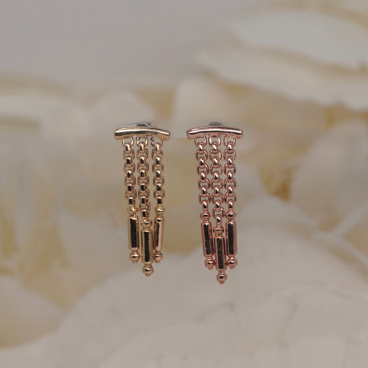 Tempo Hidden Helix textured chains and polished rectangular accents yellow gold rose gold, photographed against a soft blurred cream floral background.