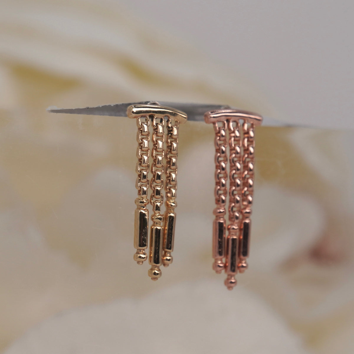 Tempo Hidden Helix textured chains and polished rectangular accents yellow gold rose gold, photographed side view against a soft blurred cream floral background.