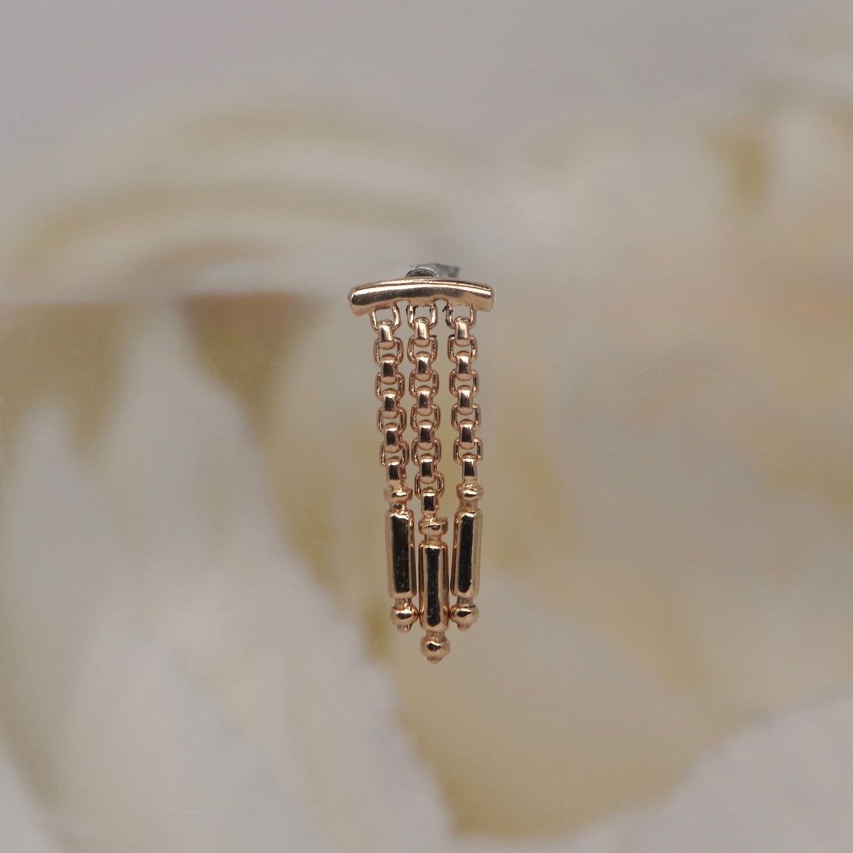Tempo Hidden Helix textured chains and polished rectangular accents yellow gold photographed against a soft blurred cream floral background.