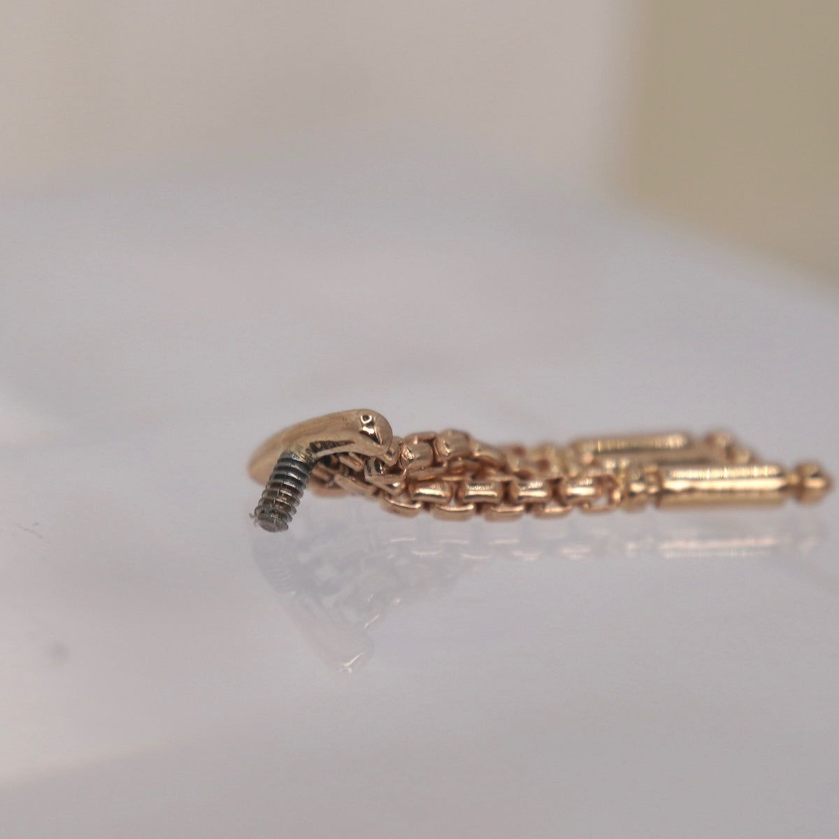Tempo Hidden Helix textured chains and polished rectangular accents yellow gold 16g threaded photographed against a soft blurred cream floral background.