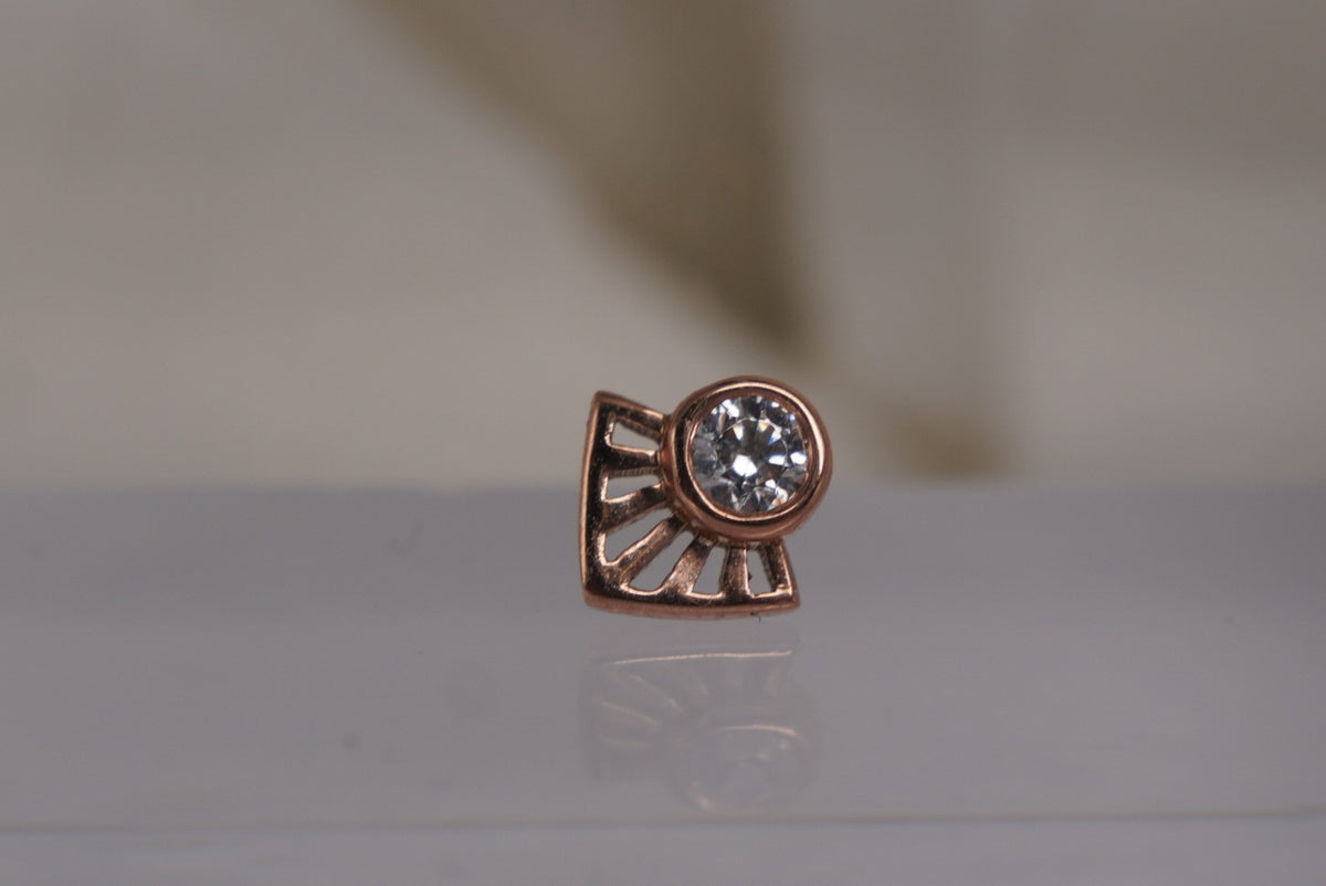 Front view of Buddha Jewelry’s “Dali” in 14k rose gold, featuring a bezel-set crystal framed by radiating angular lines.