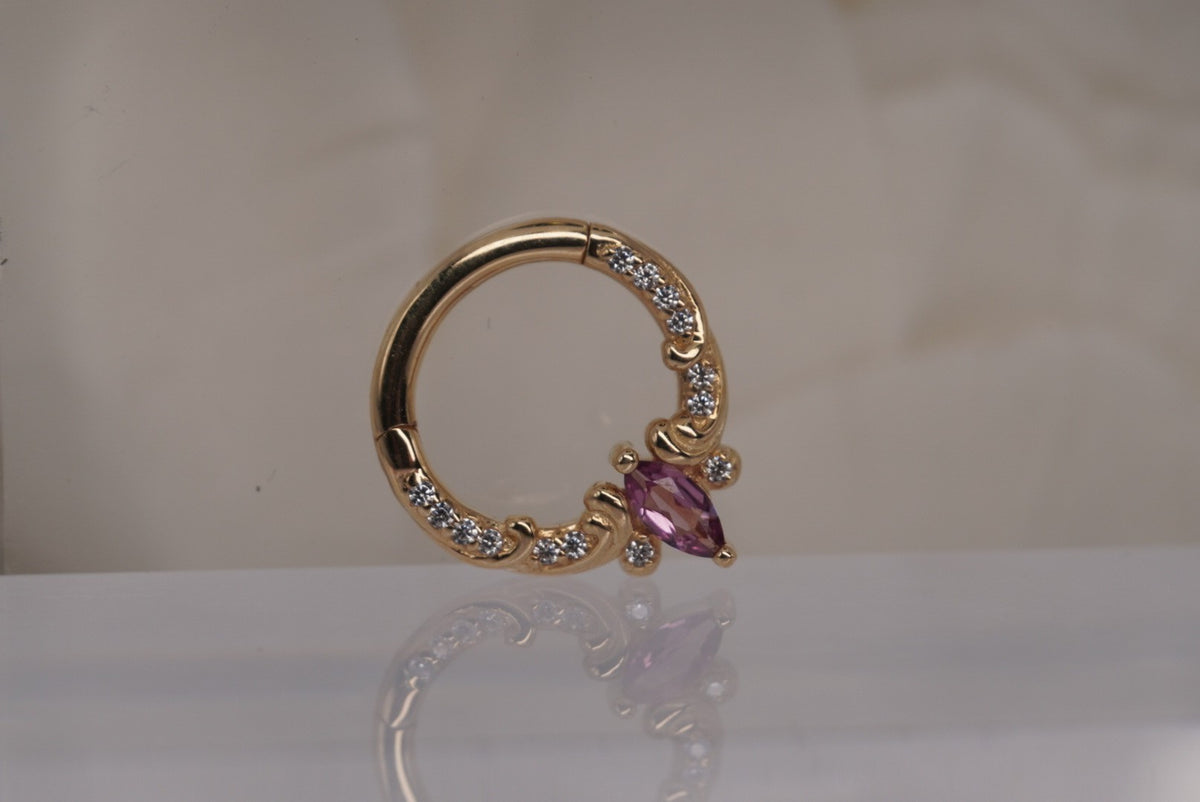 Front view of Buddha Jewelry’s “Coterie” clicker in 14k yellow gold, featuring a marquise-cut pink tourmaline accented by delicate crystals and ornate scrollwork.