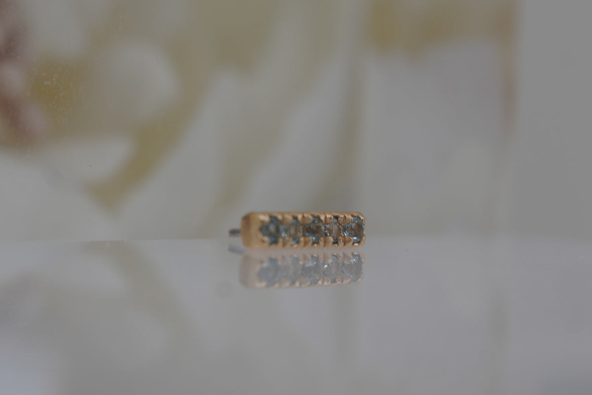 Angled view showing the blue gemstone settings along the slim gold bar.