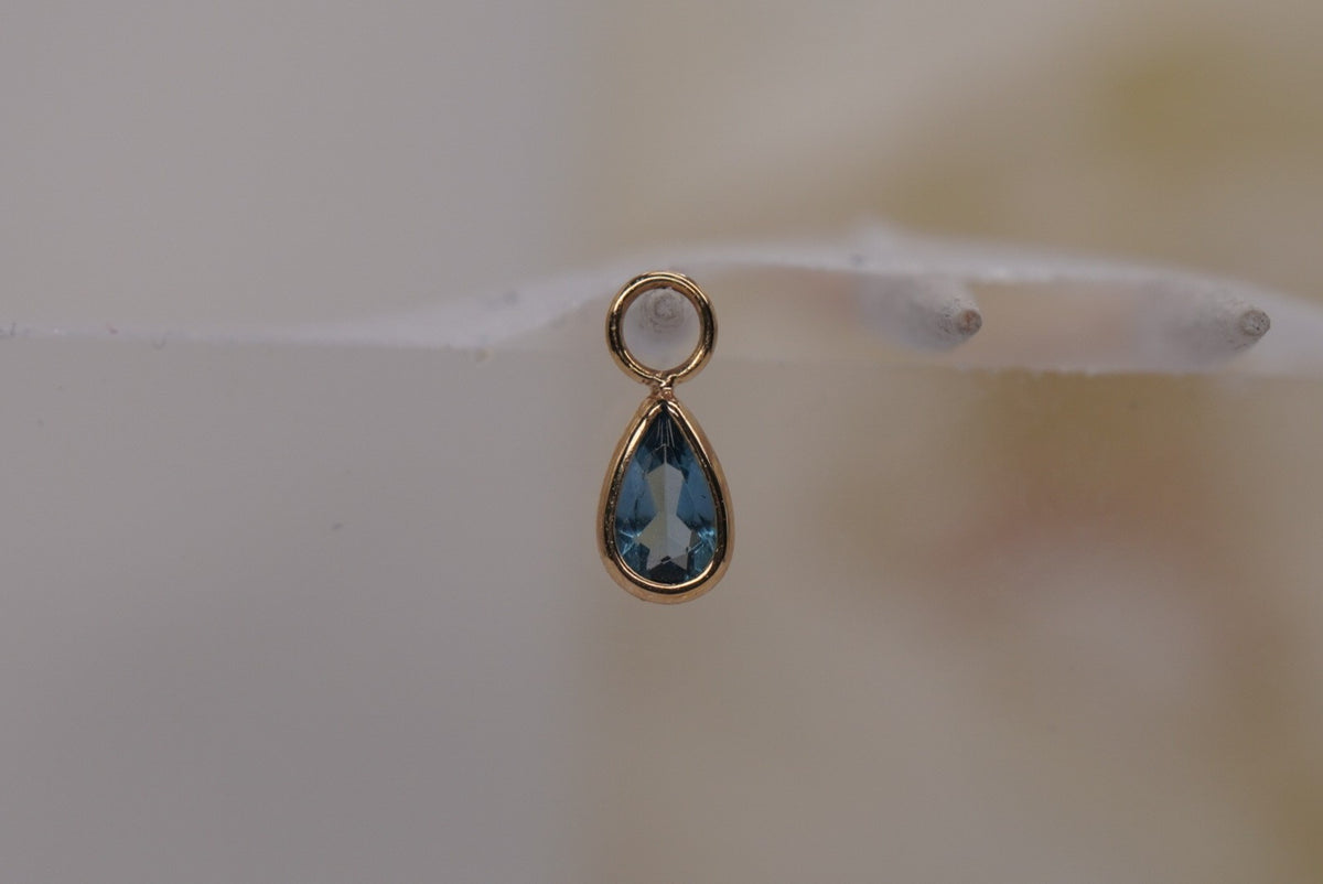 Front view of Buddha Jewelry’s “Concorde Teardrop” in 14k yellow gold, featuring a faceted London Blue Topaz drop in a smooth gold setting.