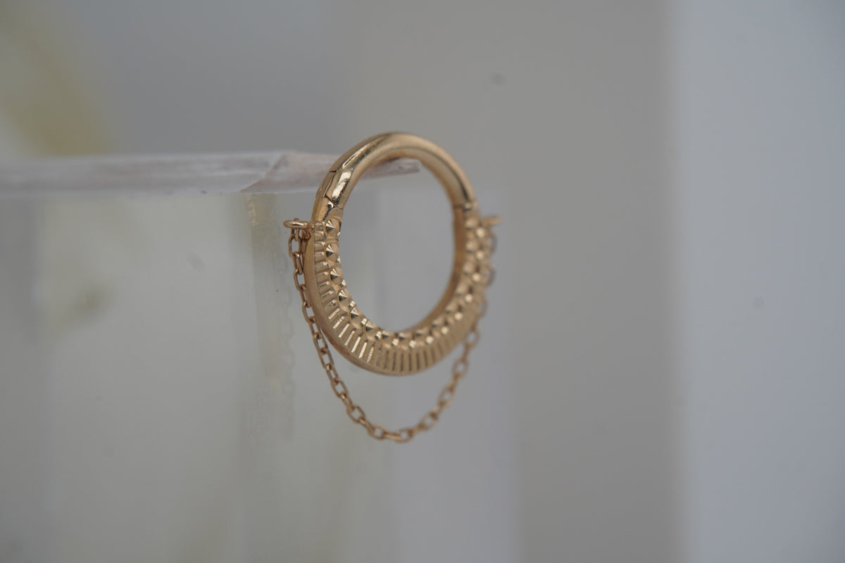 Angled view showing the clicker’s textured gold design and chain.