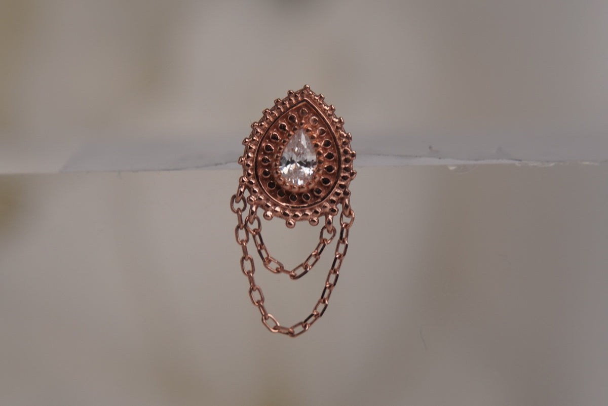 Front view of Buddha Jewelry’s “Deity” in 14k rose gold, featuring a luminous center crystal framed by ornate goldwork with delicate chains draped below.