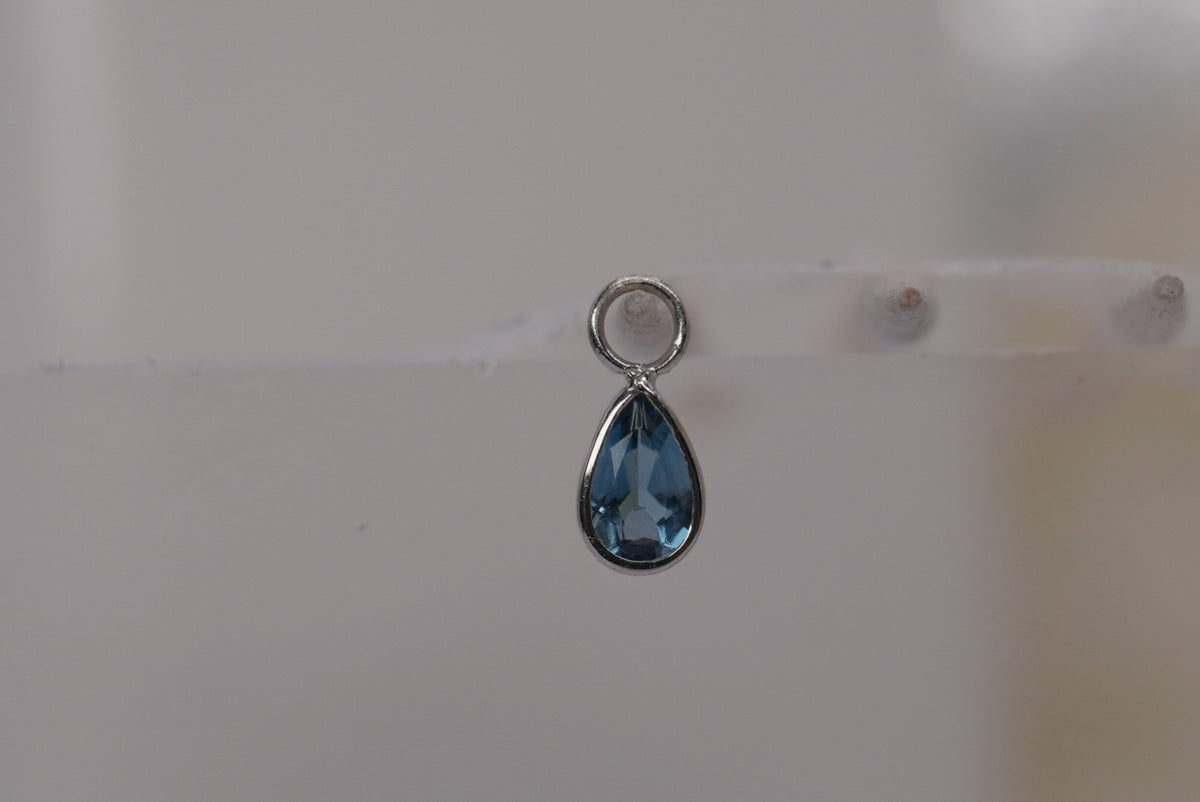 Front view of Buddha Jewelry’s “Concorde Teardrop” in 14k white gold, featuring a faceted London Blue Topaz drop in a smooth gold setting.