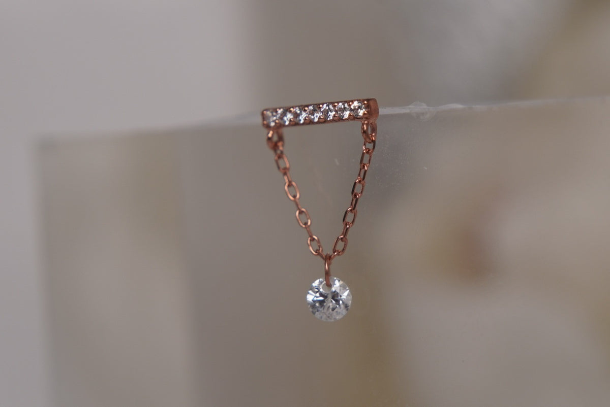 Angled view of Buddha Jewelry’s “Dolce” dangle in 14k rose gold, featuring a crystal-lined bar above a delicate chain and single drop.