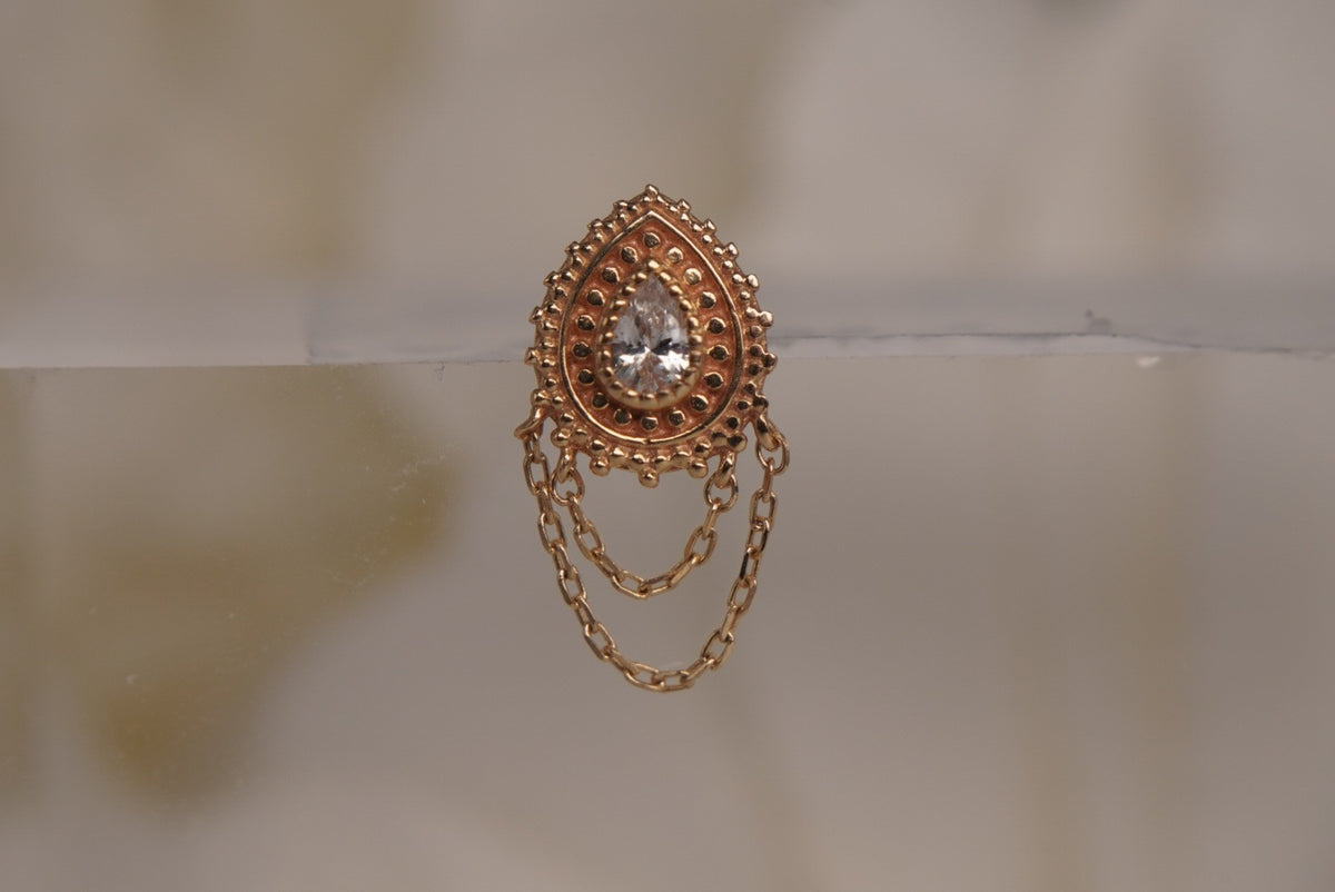 Front view of Buddha Jewelry’s “Deity” in 14k yellow gold, featuring a luminous center crystal framed by ornate goldwork with delicate chains draped below.